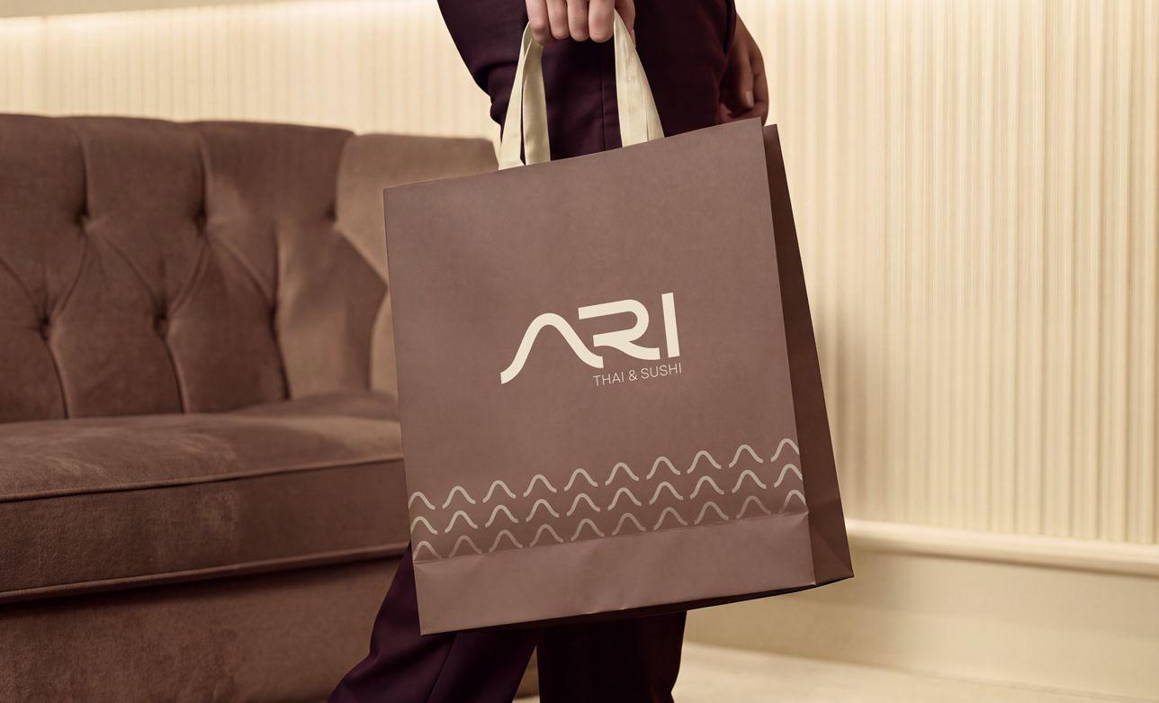 An ARI Thai & Sushi takeaway bag carried past a velvet sofa