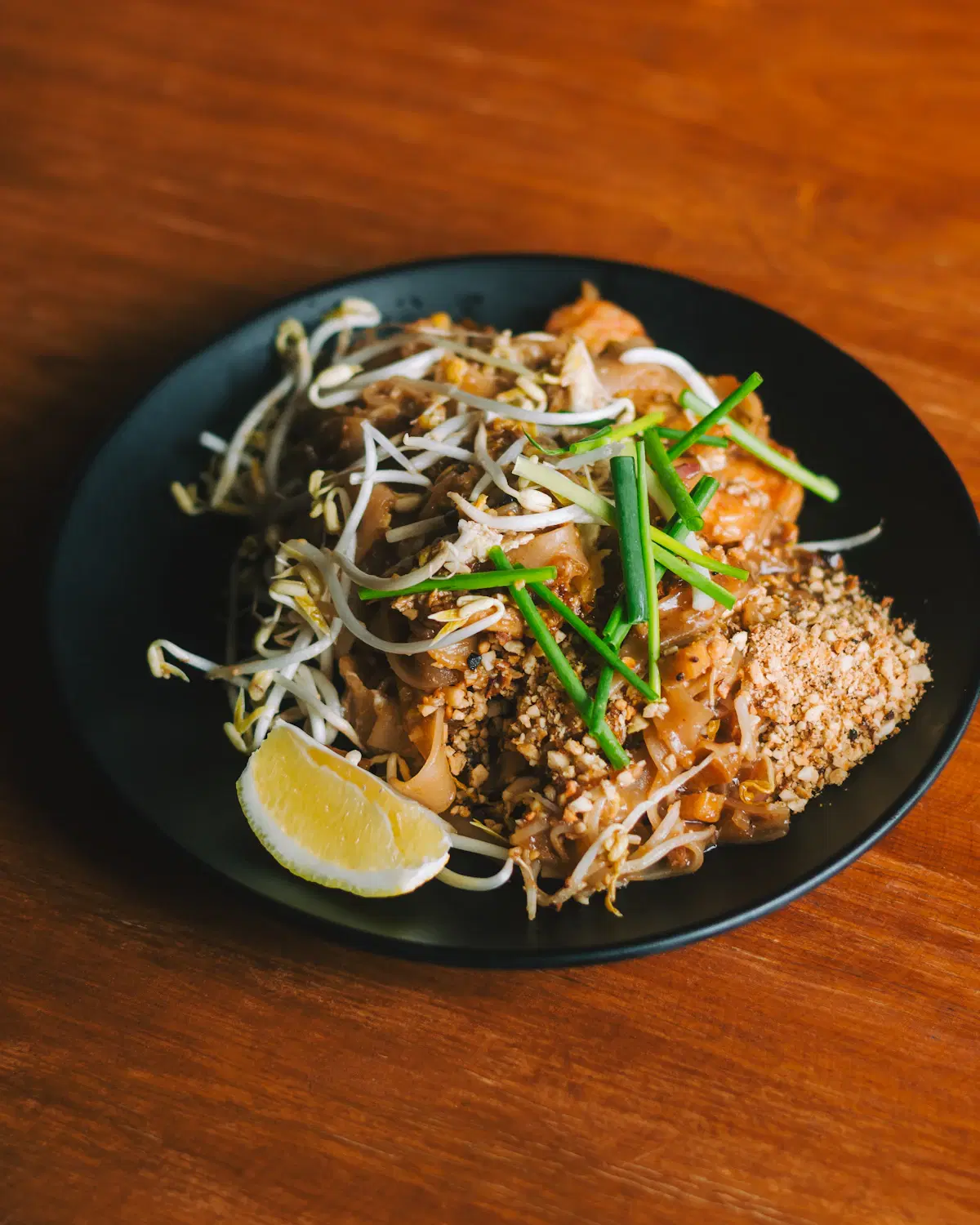 Pad Thai with rice noodles, bean sprouts, chives, crushed peanuts and a lemon wedge on a black plate