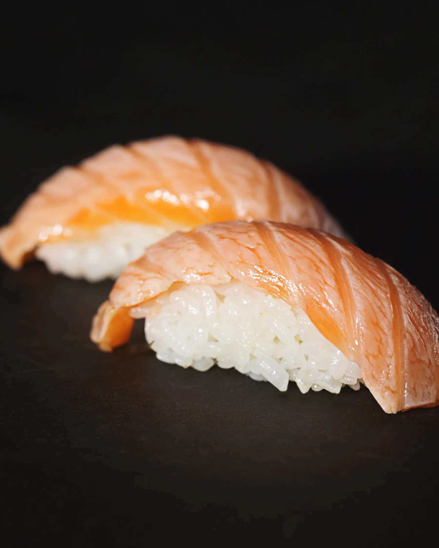 Two pieces of salmon nigiri on a dark background
