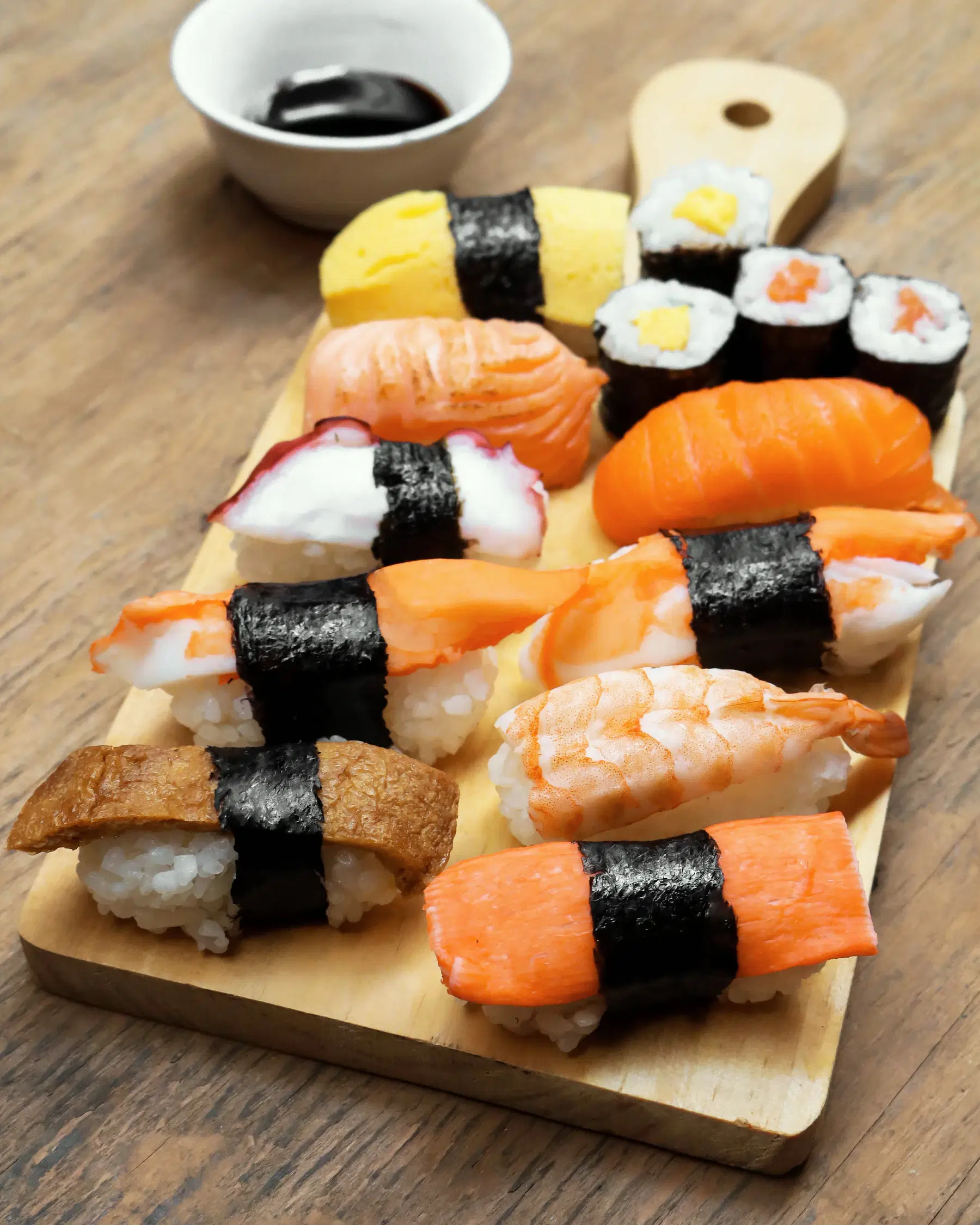 Assorted nigiri and maki on a wooden serving board with a dish of soy sauce