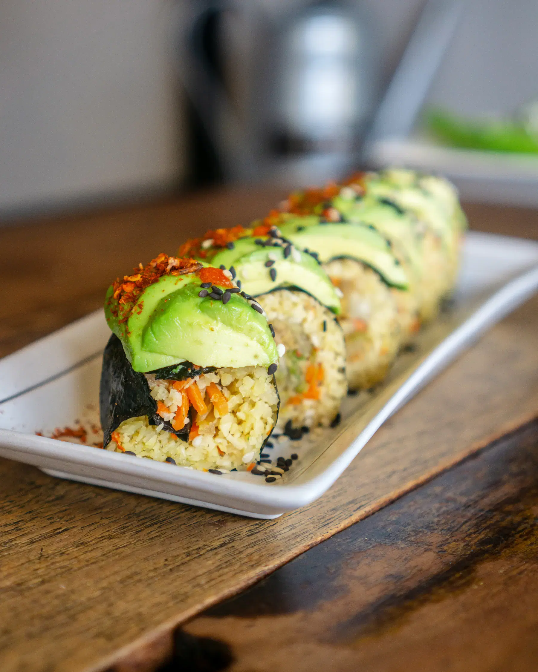 Vegan sushi rolls topped with sliced avocado, chili flakes and sesame seeds on a white plate