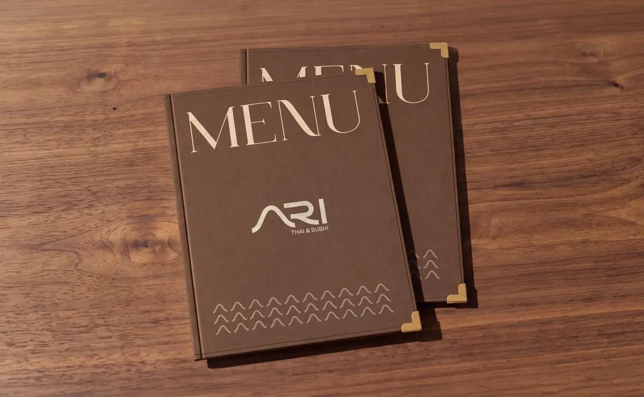 Two brown leather ARI menus with brass corners on a walnut table