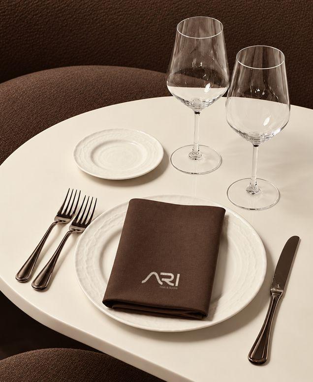 A dinner table set with a brown ARI napkin and wine glasses