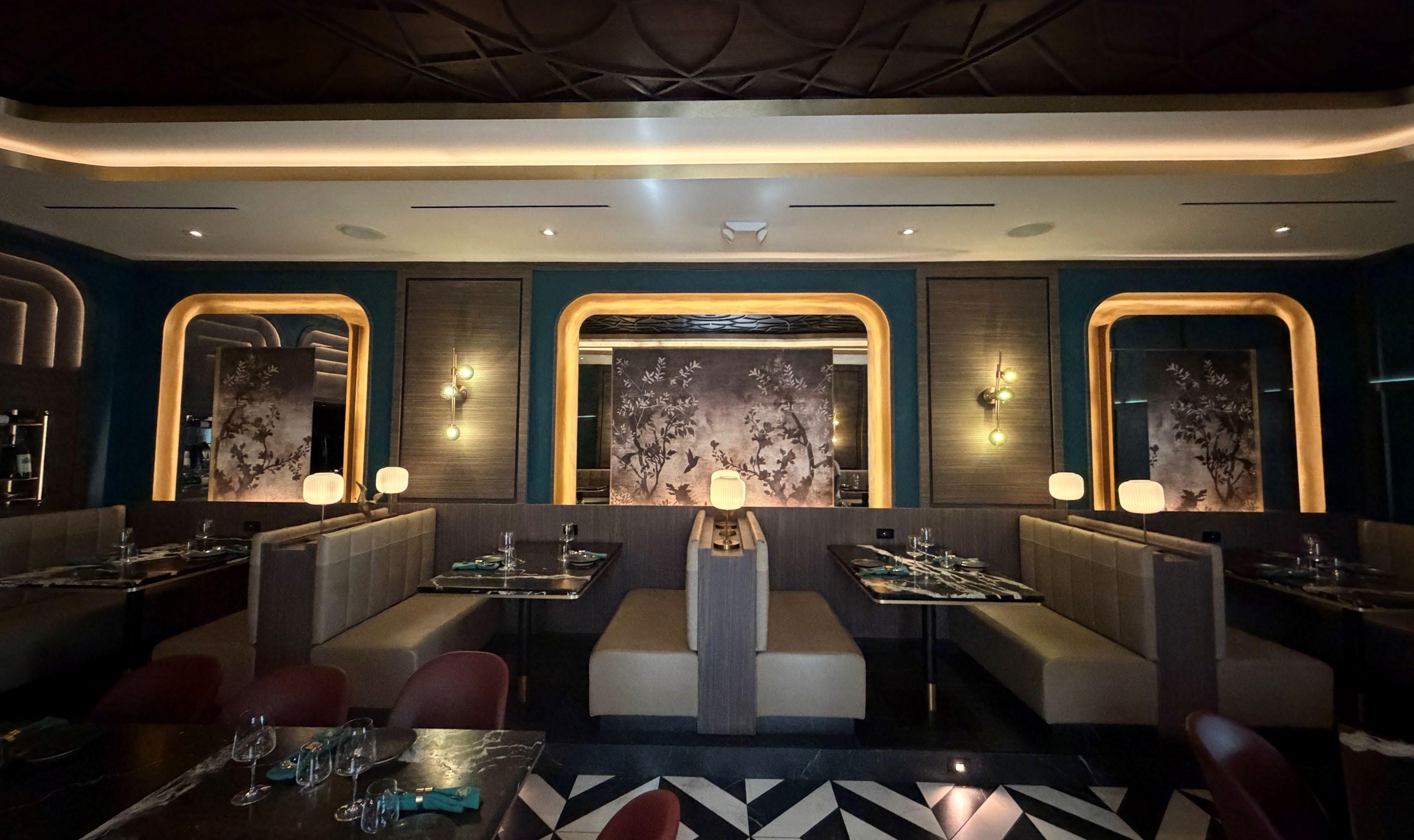 Booths beneath brass-lit arches, teal walls and silk-screen blossoms
